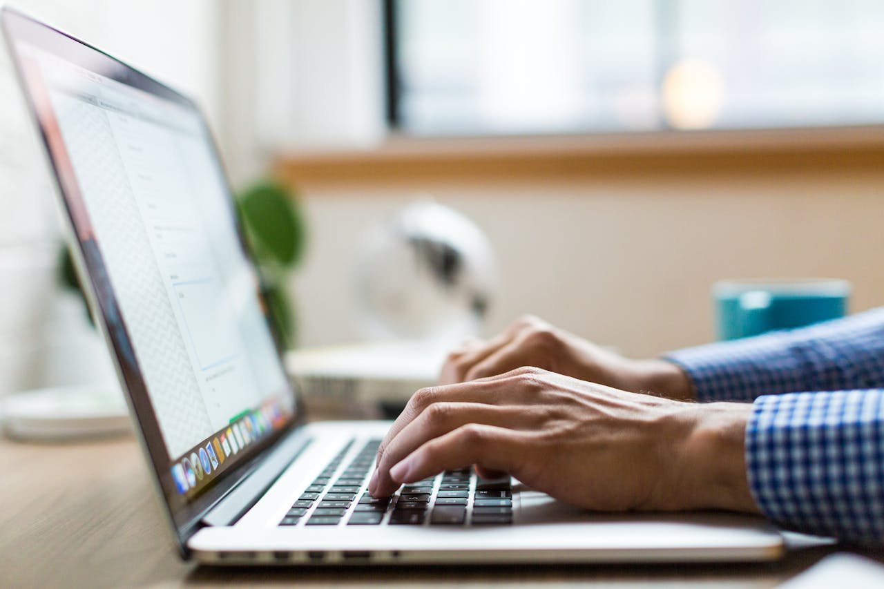 Close-up of adult typing on laptop in bright, modern office.